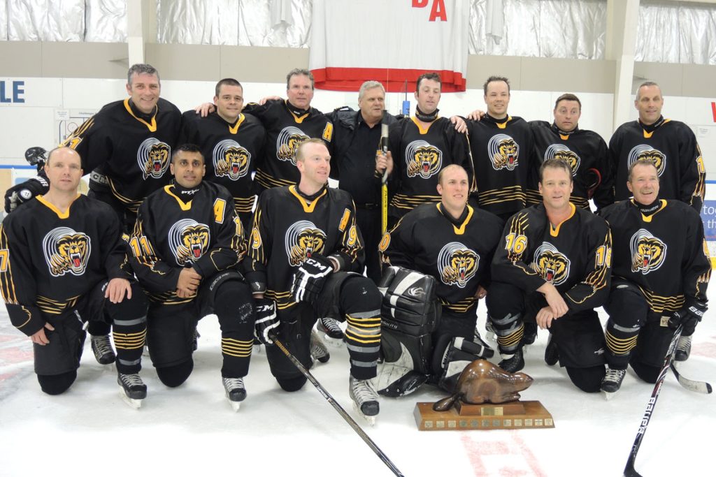The Esquimalt Fire Bear gather for a team photo after their gold medal win. Right: Fire Bears team captain Josh Peterson of Esquimalt Fire and Rescue raises the Beaver Cup trophy over his head in celebration of their win. Inset below: Blues guitarist Jesse Roper and member of the RPOps Thrashers belts out a rendition of O Canada on his guitar during the Beaver Cup opening ceremony at Wurtele Arena. Photo by Peter Mallett