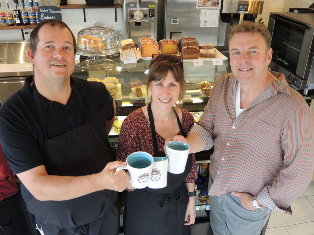 From left: Kindness Ambassador Greg Hind is joined by A Kinder Cup owners Chief Petty Officer First Class (Retired) Marc Dufort and Kim Dufort as they raise a toast to their new coffee shop at Admirals Walk Plaza. Photo by Peter Mallett