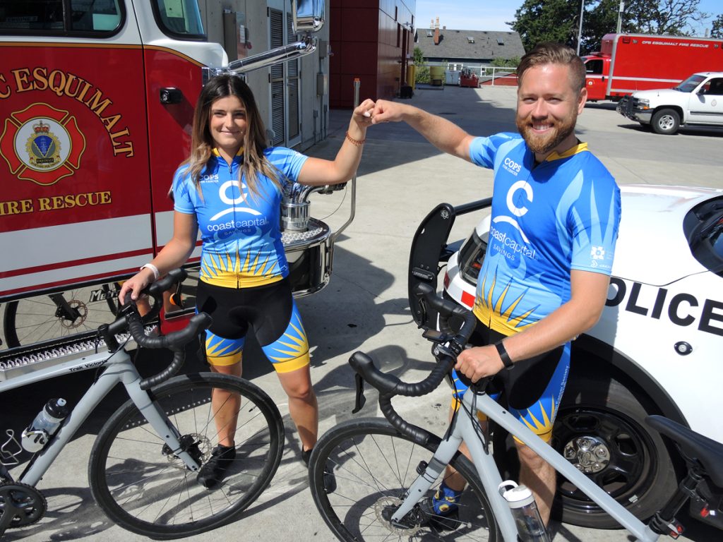 CFB Esquimalt Fire and Rescue Services Alexandria Marshall (left) and Corporal Michael Smith of Military Police Unit Esquimalt bump fists in front of emergency services vehicles. The duo will participate in the upcoming Tour de Rock fundraiser to benefit pediatric cancer