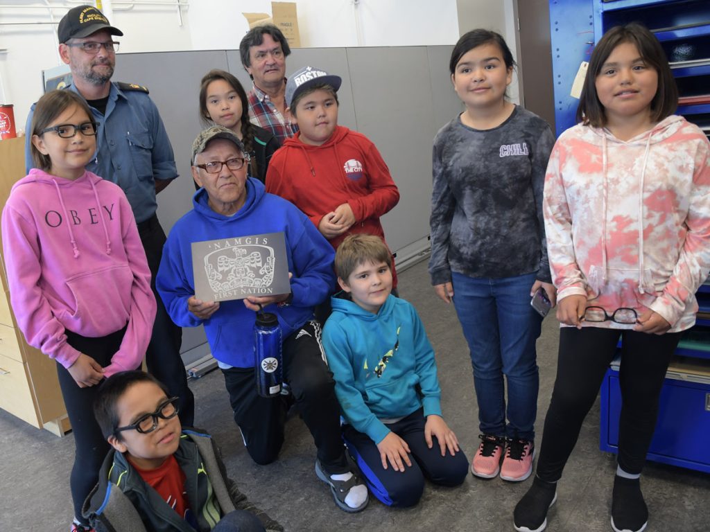 PO1 Wiggins presents Bruce Alfred an engraving of the Namgis First Nation’s logo; George Alfred and the students of T’lisalagi’lakw school pose with him in the Fleet Maintenance Facility engraving shop. Photo by SLt M.X. Déry