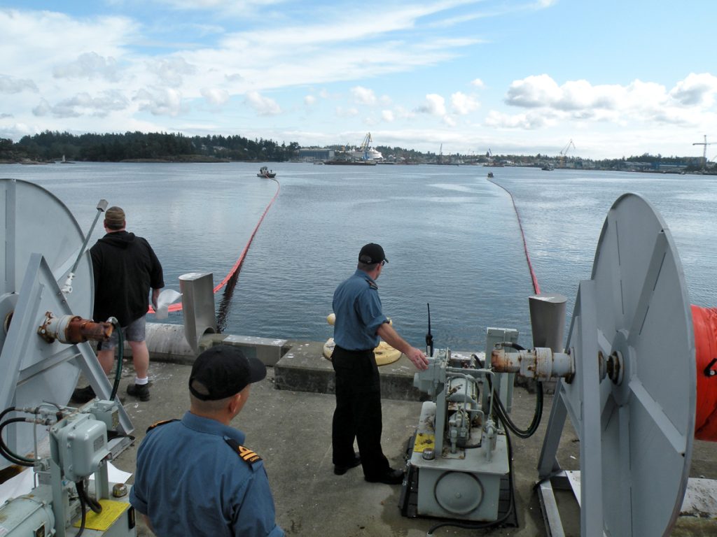 A Base Logistics employee and LS Darryl Forry of HMCS Regina deploy a containment boom from F Jetty during a spill response training exercise on Sept. 18 in Esquimalt Harbour.