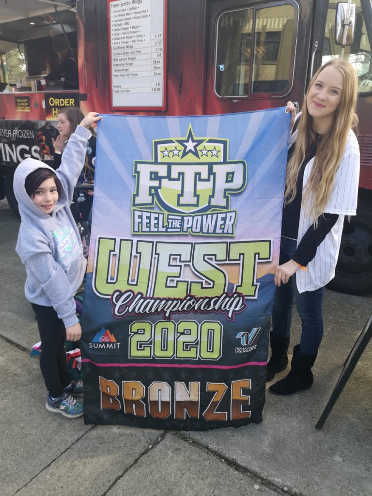 Cheerleader Jayna Flammand (left) and Pacific Cheer Empire owner and head coach Shannon Samson display Jayna’s bronze medal banner. Flammand is the eight-year-old daughter of Cpl Kevin Flammand. She won the banner for her individual performance at the Feel The Power West Coast Championship in Vancouver