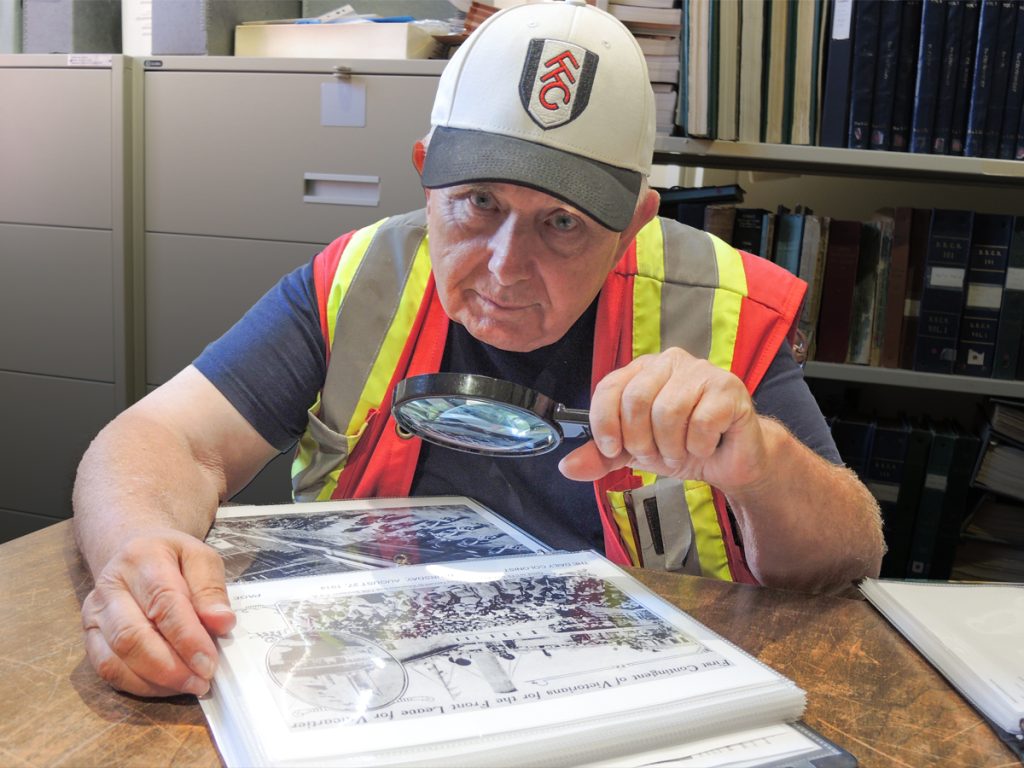 Commissionaire Gary Restell examines a photograph from 1914 depicting a march of Canadian soldiers and sailors through Dockyard at the archives of the CFB Esquimalt Naval and Military Museum.